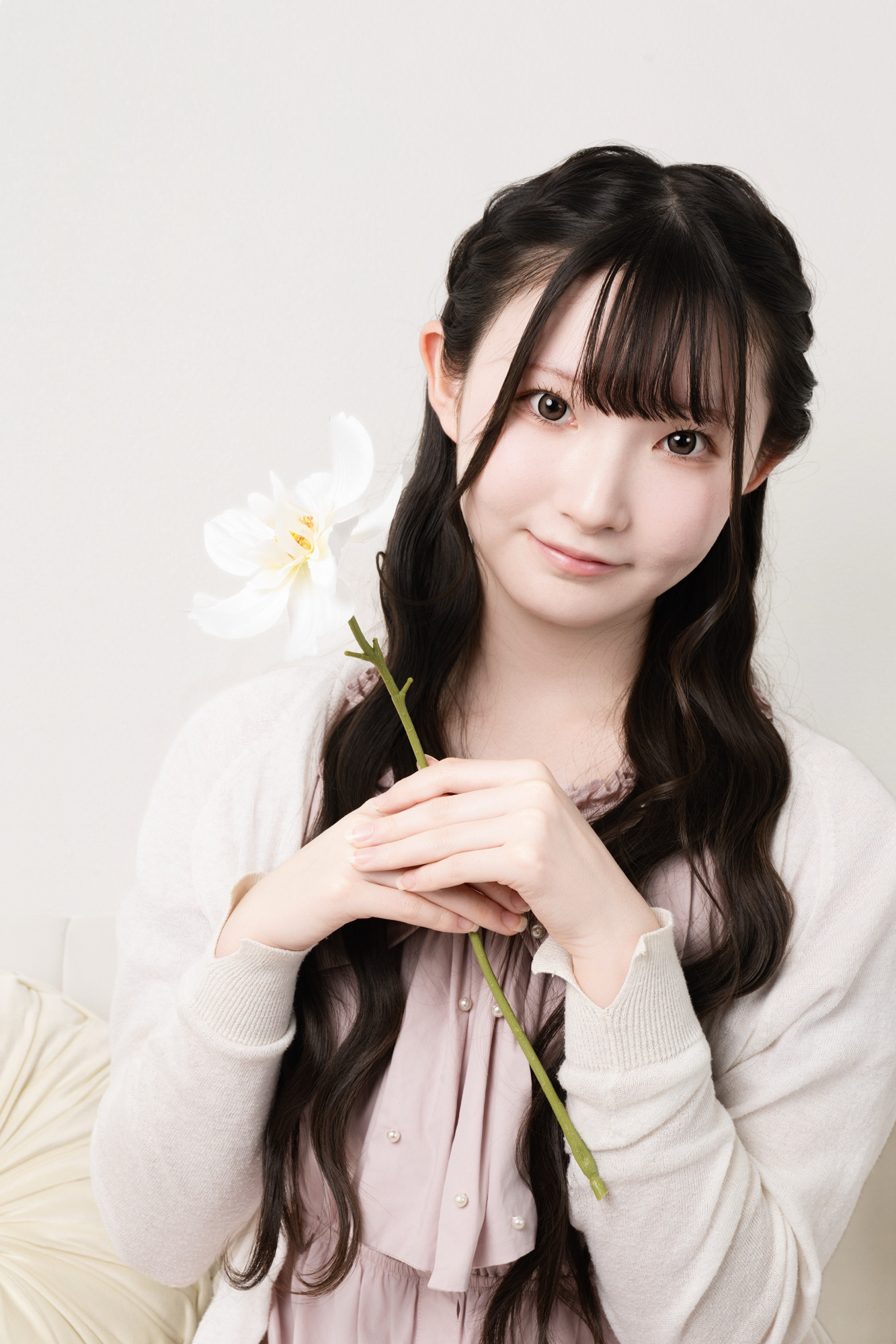 ピンクの私服で白い花を一輪持った親しみやすいプロフィール写真